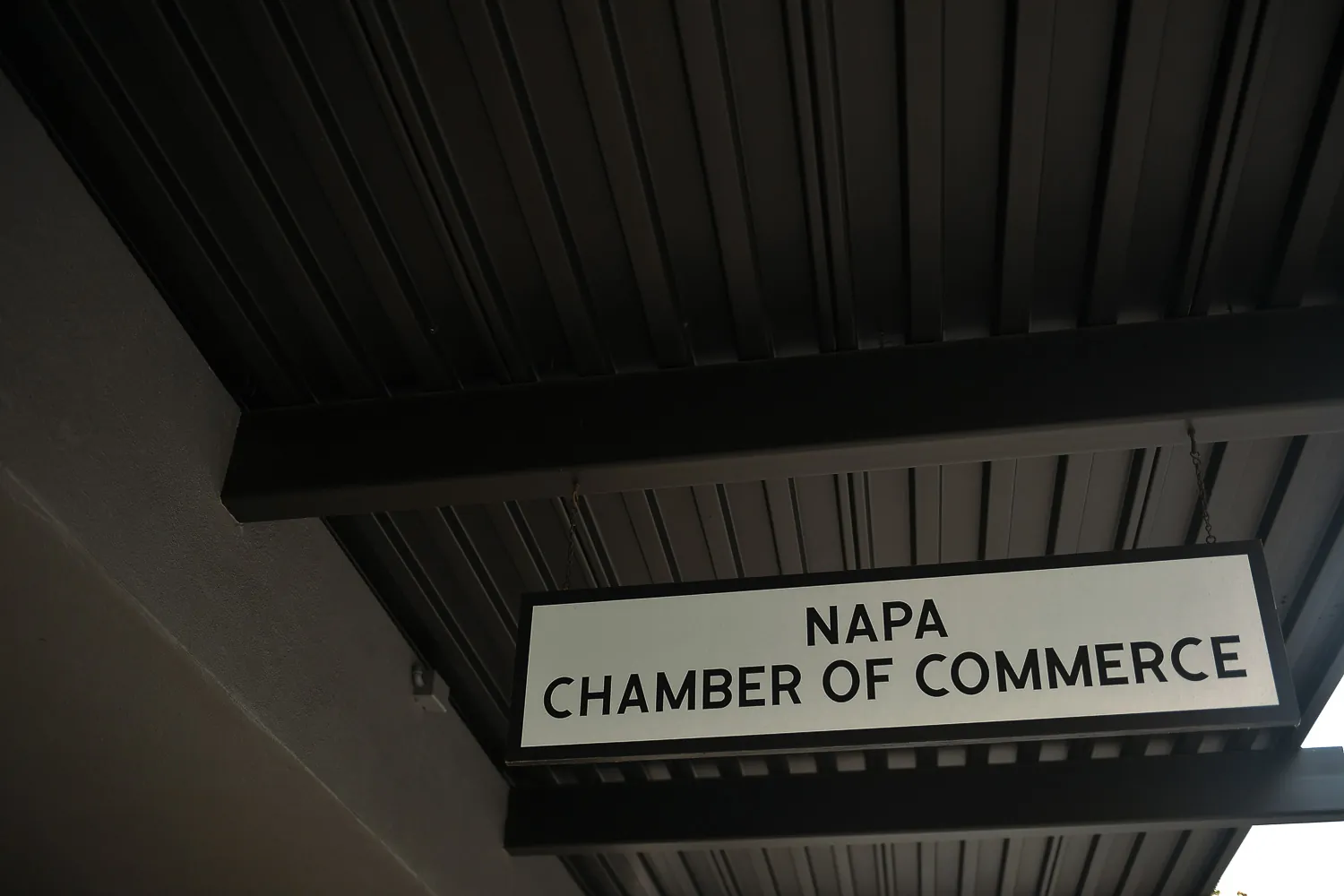A sign reading Napa Chamber of Commerce, fixed under the eave of a covered walkway.