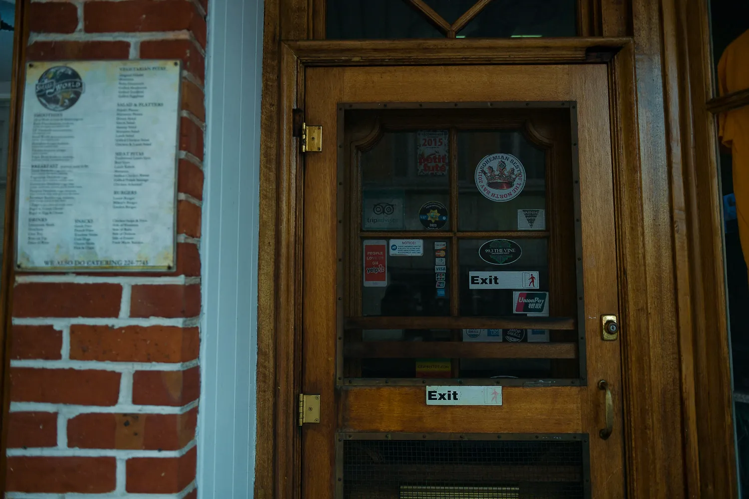 A shop door in Napa carrying a printed menu, an exit sticker and a column of review-site and guidebook badges, the most recent dated several years ago.