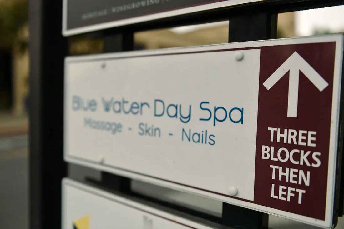 A directional sign for a day spa listing massage, skin and nails, beside an arrow marked three blocks then left.