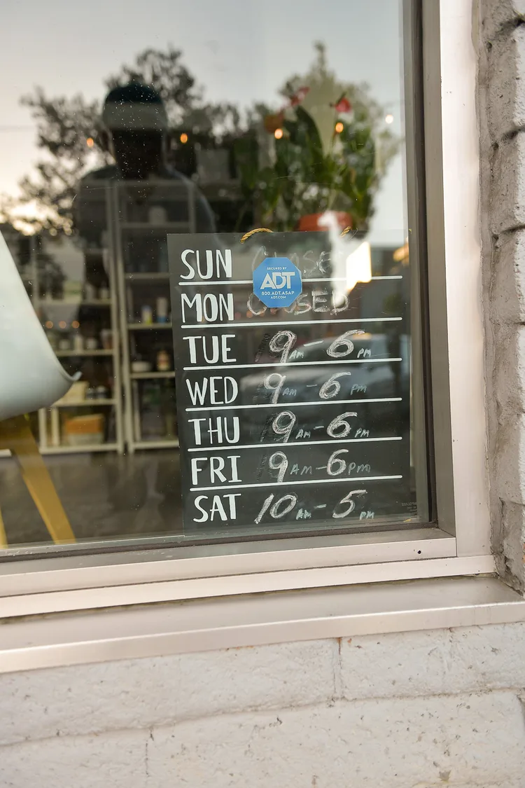 A chalkboard hung inside a shop window listing opening hours: Sunday and Monday closed, Tuesday to Friday 9am to 6pm, Saturday 10am to 5pm.