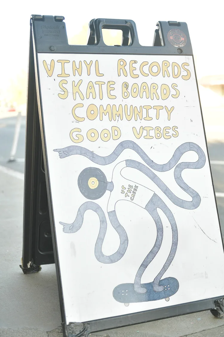 A hand-lettered sidewalk A-board reading vinyl records, skateboards, community, good vibes, with a drawing of an octopus on a skateboard.